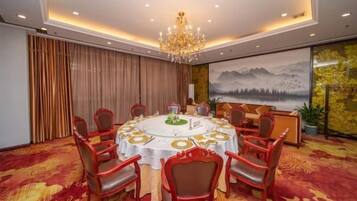 A conference room with a round table, red chairs, a chandelier, and a painting of mountains.
