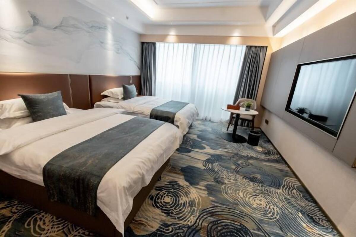 Ein Hotelzimmer mit zwei Betten, einem Schreibtisch, einem Stuhl und einem großen Fenster.