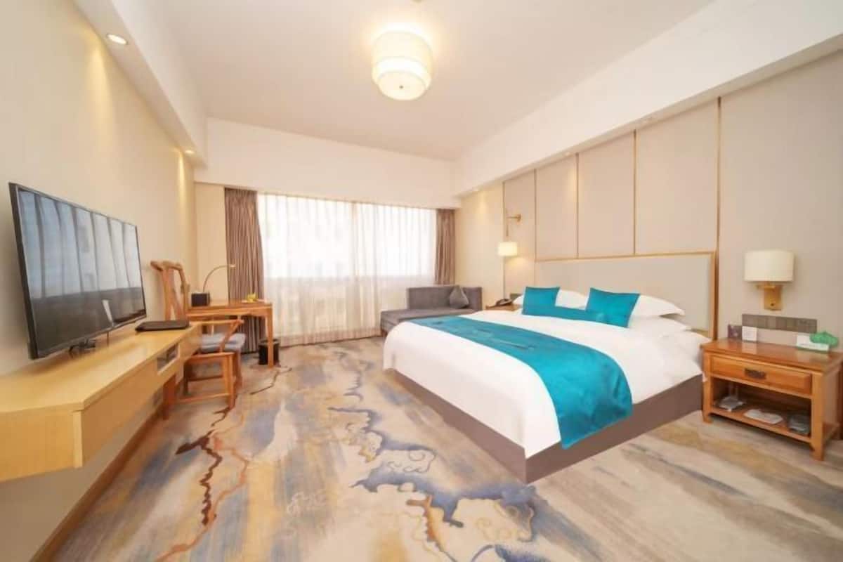 Ein Hotelzimmer mit Bett, Schreibtisch, Fernseher und einem Fenster mit Vorhängen.