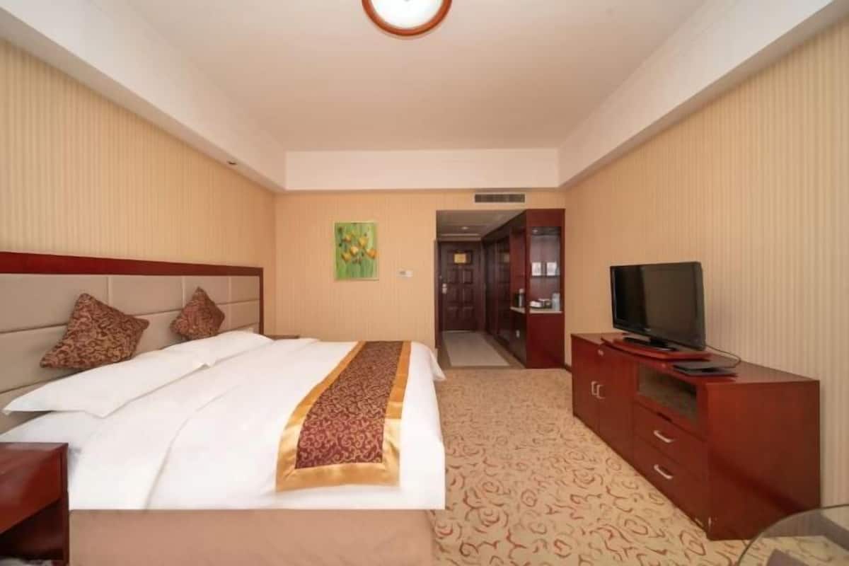 Ein Hotelzimmer mit einem Bett, einem Fernseher auf einer Holzkabine und einer Tür zu einem weiteren Raum.