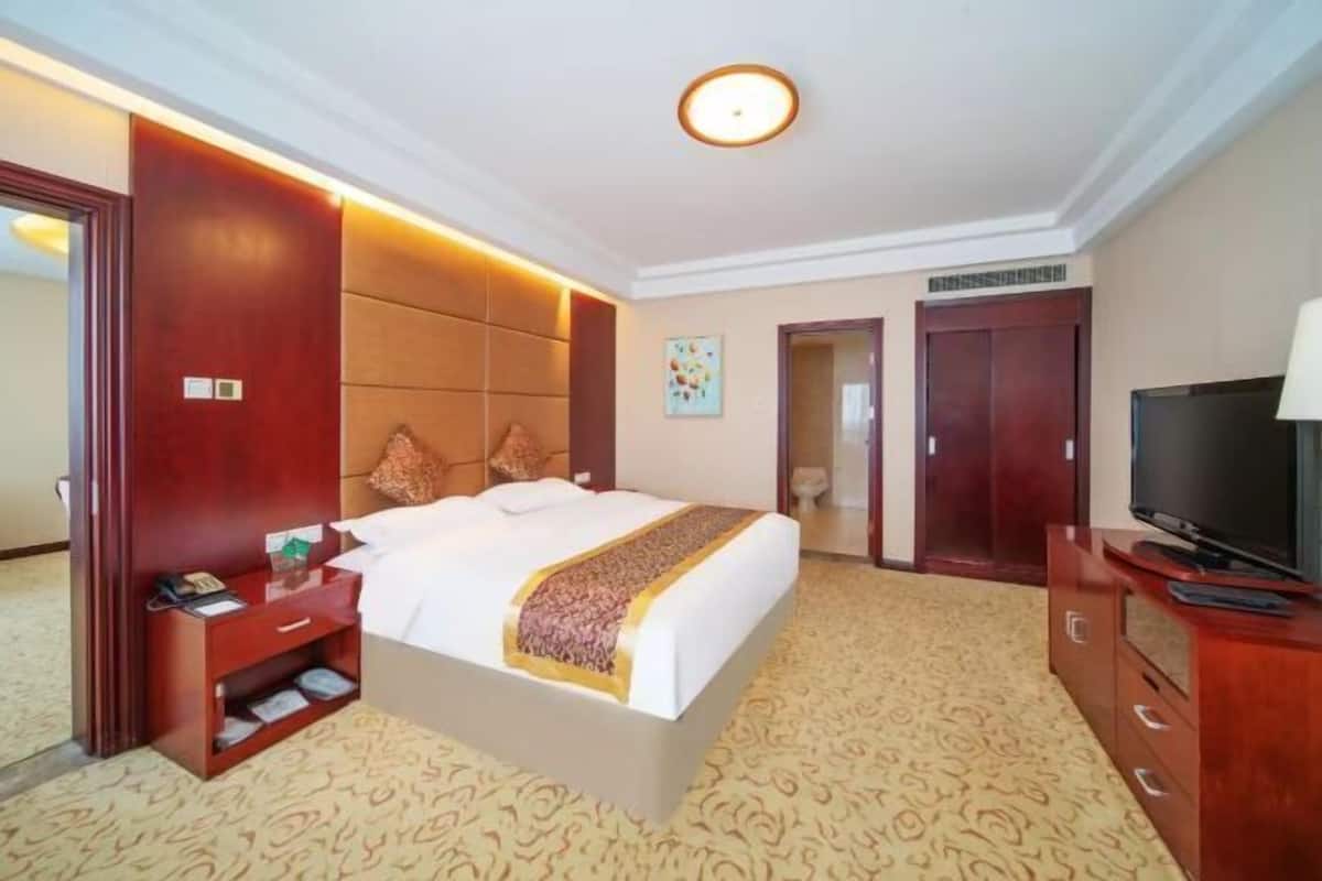 Ein Hotelzimmer mit einem großen Bett, einem Fernseher, einem Kleiderschrank und einem Nachttisch.