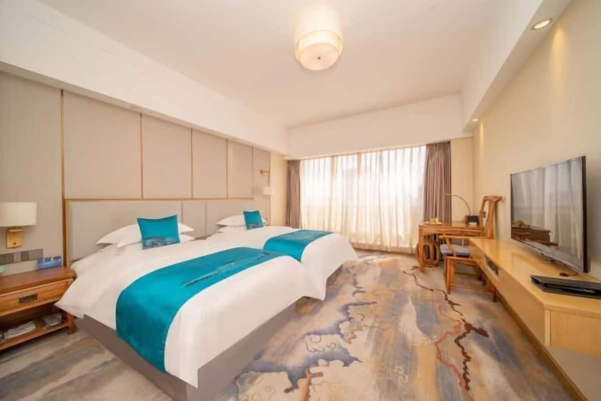 Ein Hotelzimmer mit Bett, Schreibtisch, Fernseher und einem Fenster mit Vorhängen.