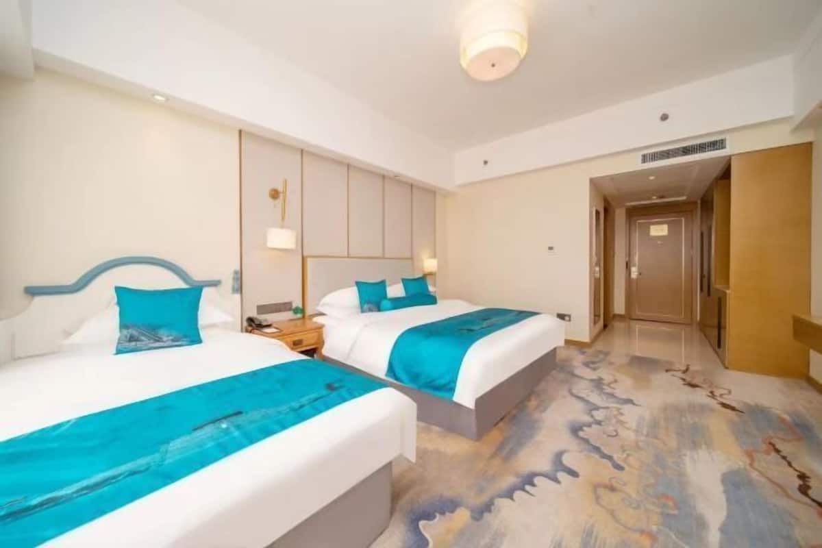 Ein Hotelzimmer mit zwei Betten, einem großen Spiegel, einem Nachttisch und Teppichboden.