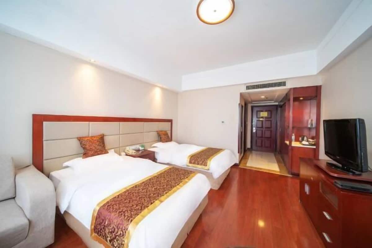 Ein Hotelzimmer mit zwei Betten, einem Fernseher, einer Couch und einem Flur, der zu einem Badezimmer führt.