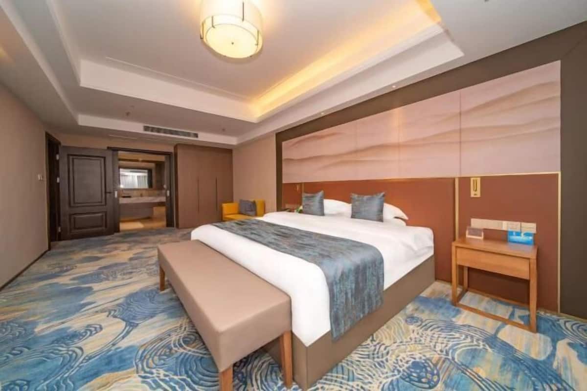 Ein Hotelzimmer mit einem großen Bett, einer Bank, einem Nachttisch und einem Kopfteil mit einer Leuchte.