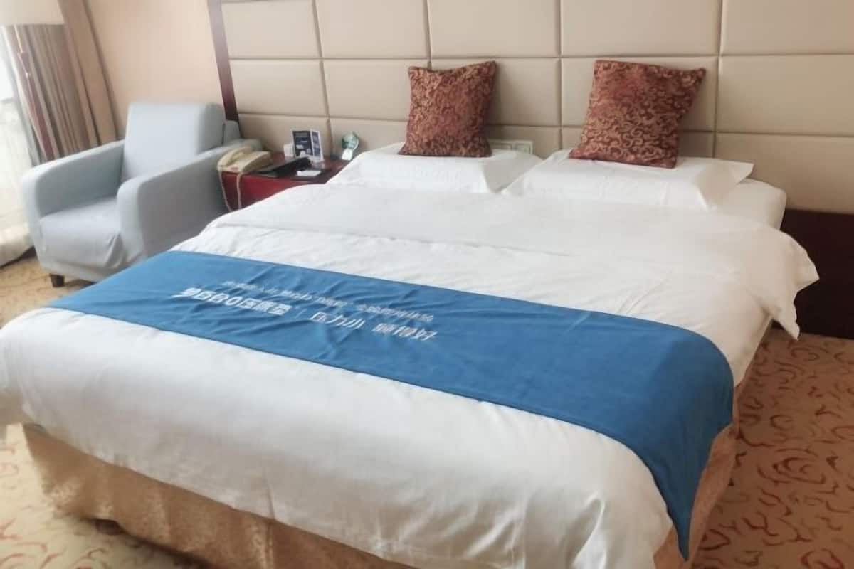 Ein Hotelzimmer mit einem großen Bett, zwei Kissen, einem Nachttisch mit Telefon und einem Sessel.