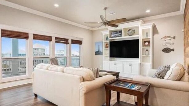A spacious living room with a large window, a ceiling fan, and a flat-screen TV mounted on a white cabinet. - Boaters' paradise, direct access to the Intracoastal, East Bay and Gulf. (Bolivar Peninsula)