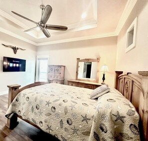 Una camera da letto con un letto, un ventilatore a soffitto, una TV, una cassettiera e uno specchio.