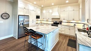 A modern kitchen with white cabinets, a stainless steel refrigerator, a microwave, and a large island with bar stools. - Boaters' paradise, direct access to the Intracoastal, East Bay and Gulf. (Bolivar Peninsula)