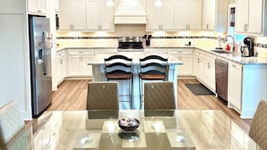 A modern kitchen with white cabinetry, a glass dining table, and two black chairs. - Boaters' paradise, direct access to the Intracoastal, East Bay and Gulf. (Bolivar Peninsula)