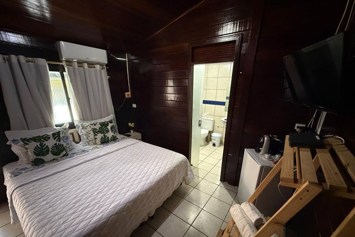 A bedroom with a bed, curtains, a television, and a bathroom visible through an open door.