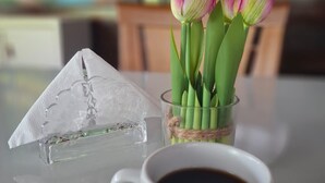 A clear glass pyramid, a glass vase with pink tulips, and a white mug with coffee on a table. - Pousada das Flores (Fernando de Noronha)