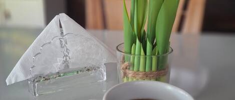 A clear glass pyramid, a glass vase with pink tulips, and a white mug with coffee on a table.