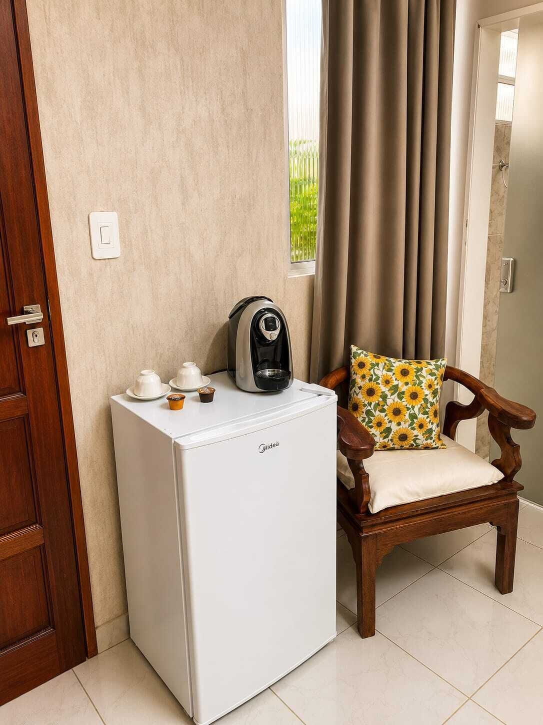 Um eletrodoméstico branco e compacto, possivelmente um mini-refrigerador, com uma cafeteira em cima, uma porta de madeira e uma cadeira com almofada de girassol.
