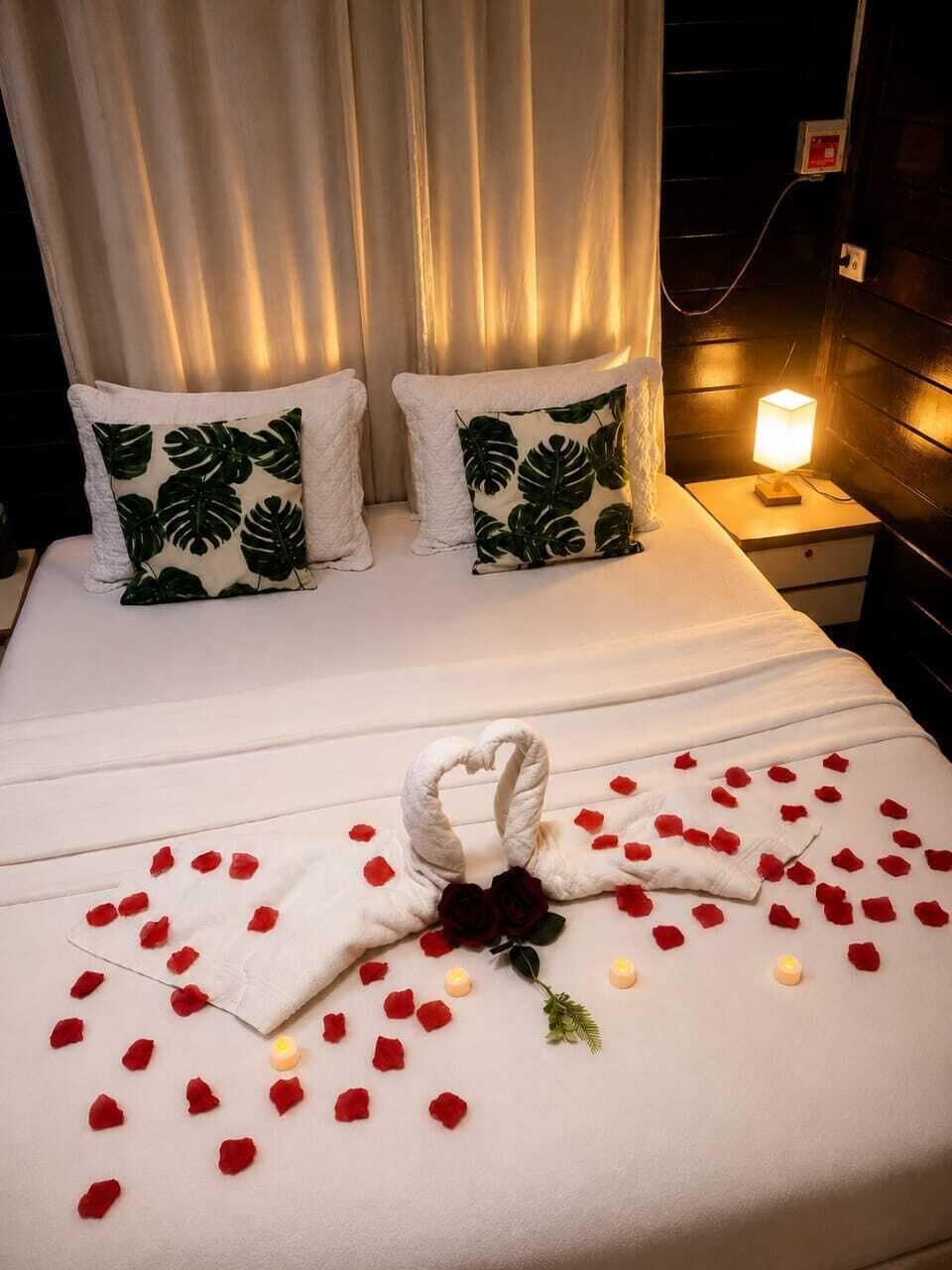 Un lit décoré d’une serviette en forme de cœur, de pétales de rose et d’une bougie.