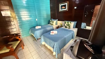 Quarto com duas camas, uma cadeira de madeira, uma mesinha e um espelho.