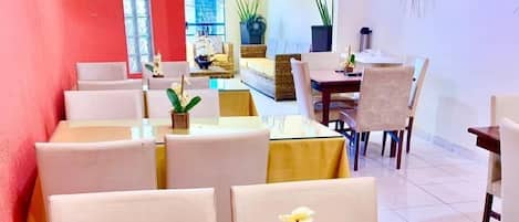 Un coin repas avec une table en verre, des chaises blanches et un petit arrangement floral composé d’orchidées.