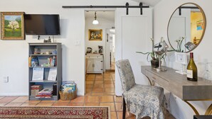 A living room with a TV, bookshelf, chair, and a dining table with a wine bottle.