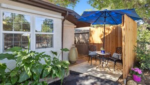 A patio with a wooden fence, a table with chairs, and a blue umbrella.