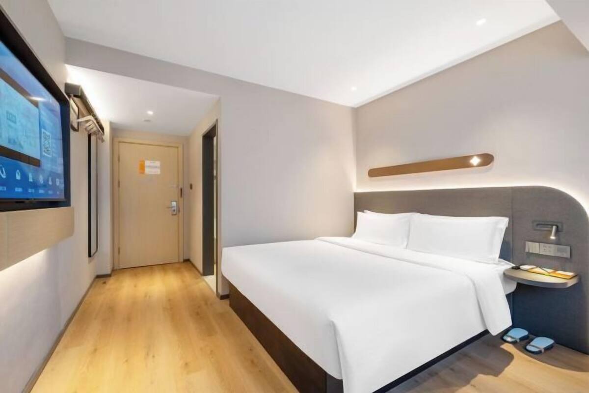 A modern hotel room with a bed, bedside table, and a TV mounted on the wall.