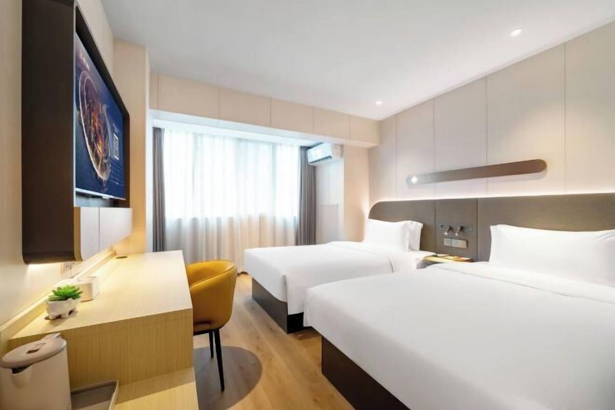 A hotel room with two beds, a desk, a chair, a TV, and a window with curtains.