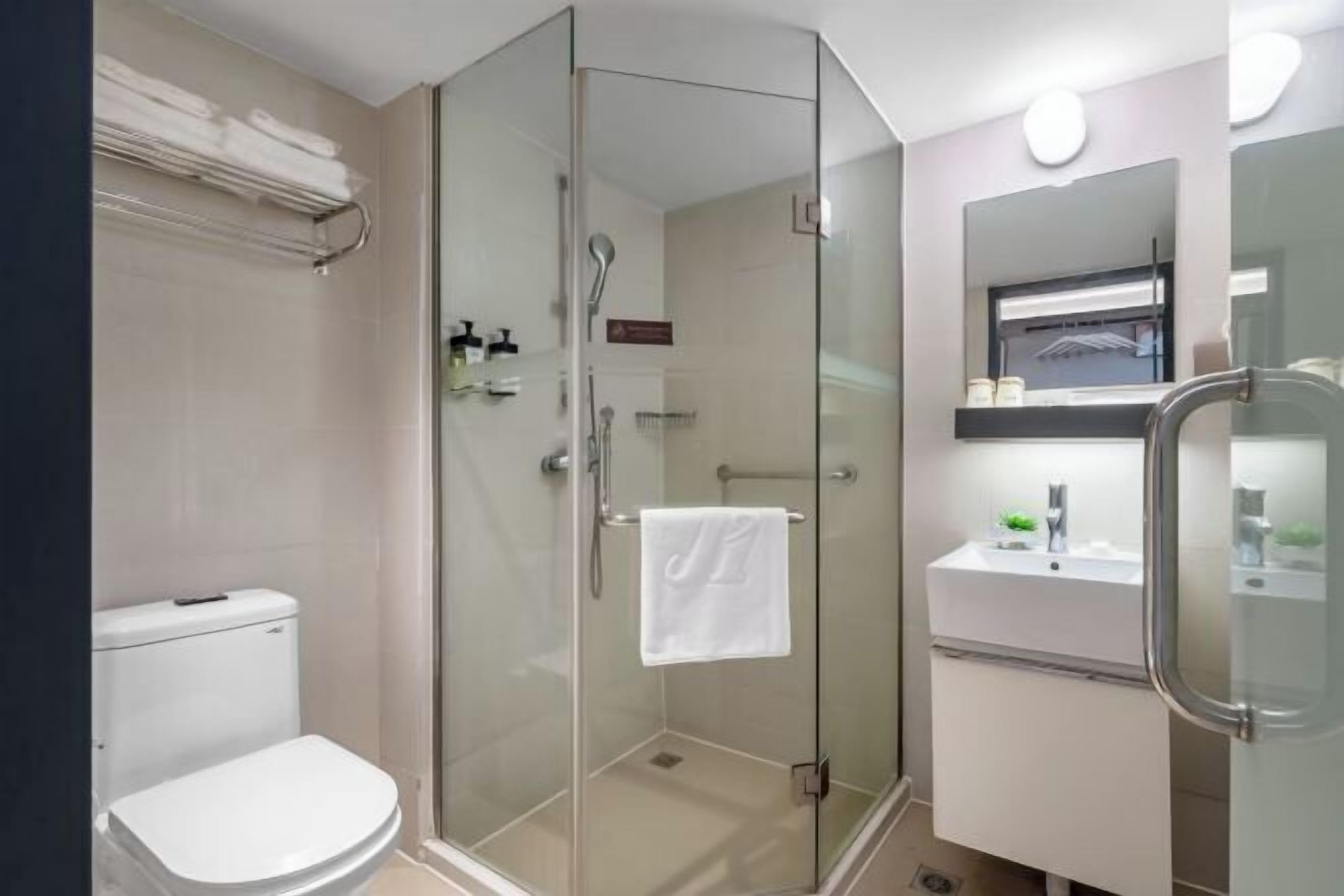 A modern bathroom with a glass-enclosed shower, a white toilet, and a sink with a mirror above it.