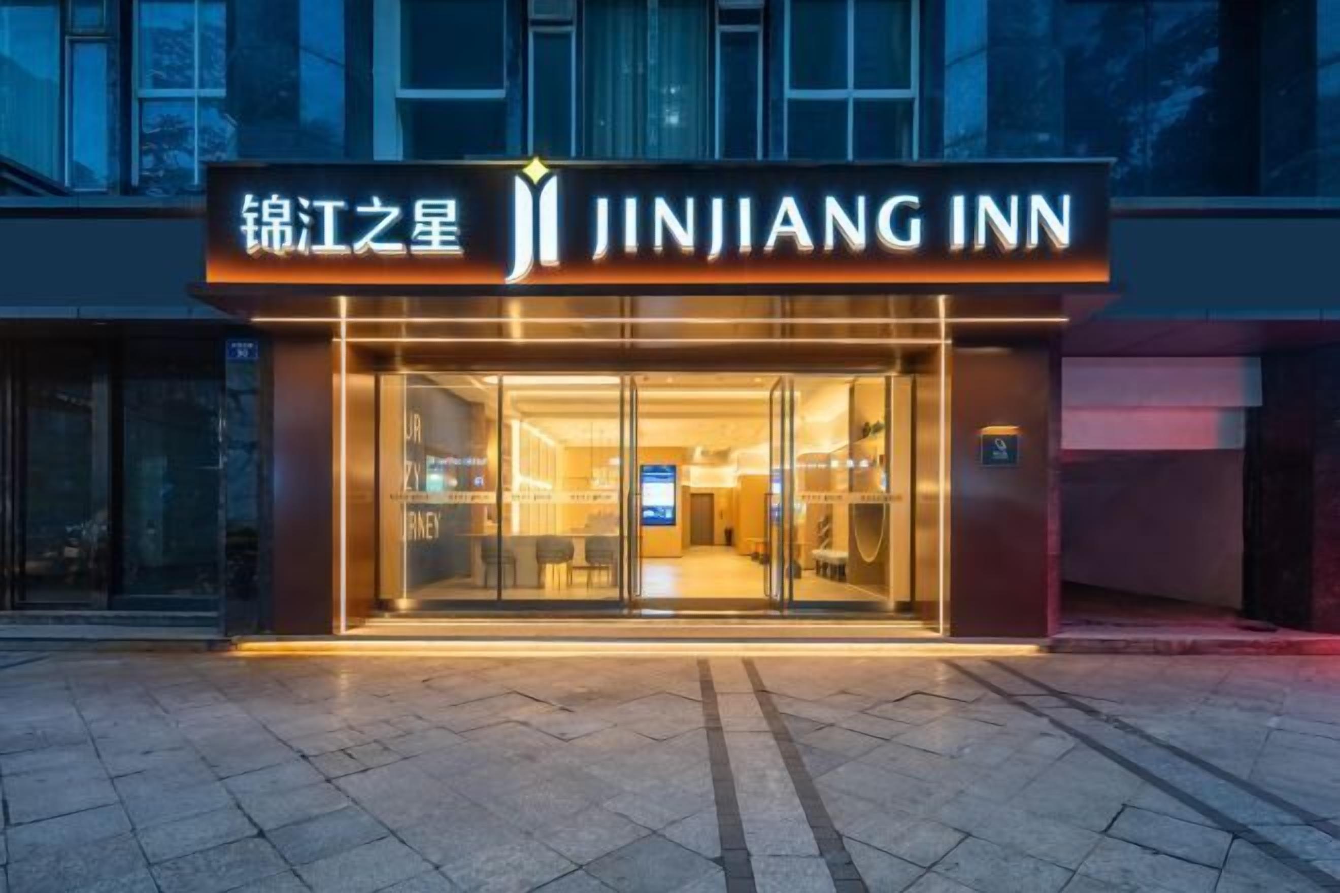 The exterior of Jinjiang Inn with a modern facade, large glass entrance, and illuminated signage.
