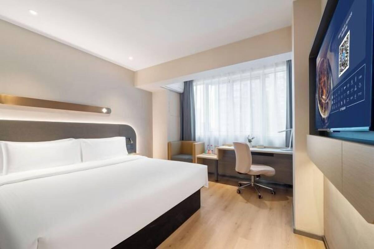 A modern hotel room with a large bed, a desk, and a chair.