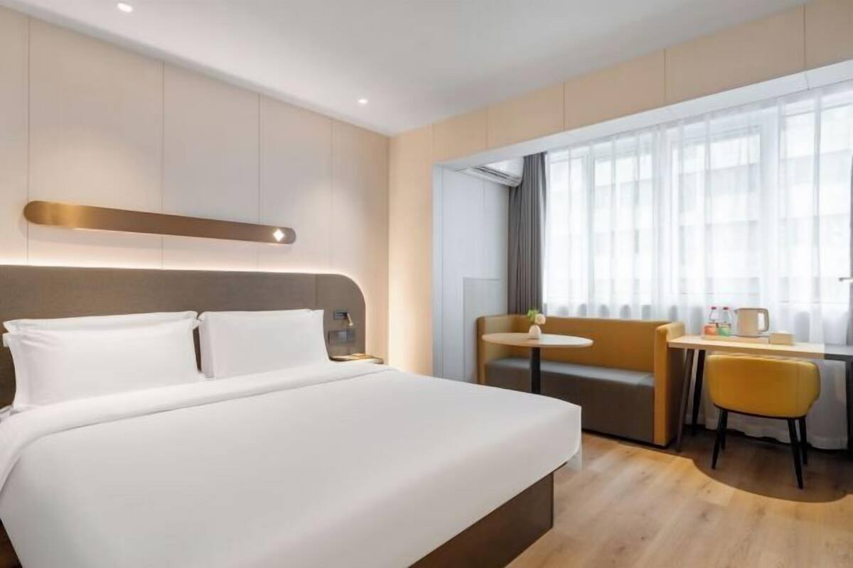 A hotel room with a large bed, a small table with chairs, and a window with curtains.