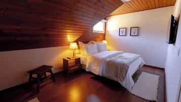 A bedroom with a wooden ceiling, a bed with white bedding, two bedside lamps, a small wooden stool, and a rug on the floor.