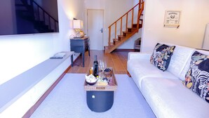 A modern living room with a sofa, a coffee table with snacks and drinks, a TV, and a staircase leading to another level. - Zur Suítes (Campos do Jordão)