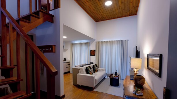 A spacious living area with a wooden staircase, a white sofa, a coffee table, and a lamp. - Zur Suítes (Campos do Jordão)