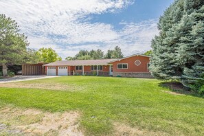 A two-story house with a garage, a well-maintained lawn, and a large evergreen tree. - Tanglewood: Dog-Friendly Retreat + Spacious Yard (Grand Junction)