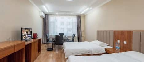 A hotel room with two beds, a wooden desk, a television, and a dining area with a table and chairs.