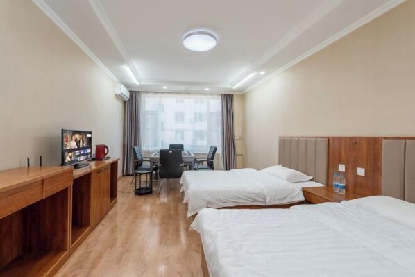 A hotel room with two beds, a wooden desk, a television, and a dining area with a table and chairs.