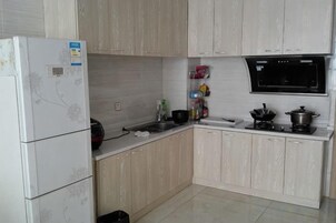 A kitchen with light wood cabinets, a white refrigerator, a stove, and various kitchen items.