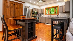 A modern kitchen with wooden cabinets, a central island, and a dining area. - Private Hilltop Retreat | Hot Tub & 15 Min to Nashville3BR, 3.5 BA (Nashville)