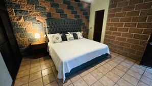 A bedroom with a bed, a nightstand, a lamp, and a brick wall. - Hotel La Roca  (Ezequiel Montes)
