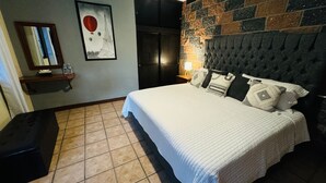 A bedroom with a large bed, a stone wall, a mirror, and a framed picture of a hot air balloon. - Hotel La Roca  (Ezequiel Montes)