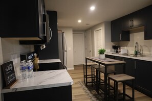 A modern kitchen with black cabinets, a marble countertop, and a small island with bar stools. - Cozy entire 2 bedroom apartment located in the heart of Mahogany. Pet friendly. (Calgary)
