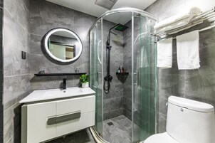 Un baño moderno con ducha de vidrio, espejo redondo, lavamanos blanco y retrete.