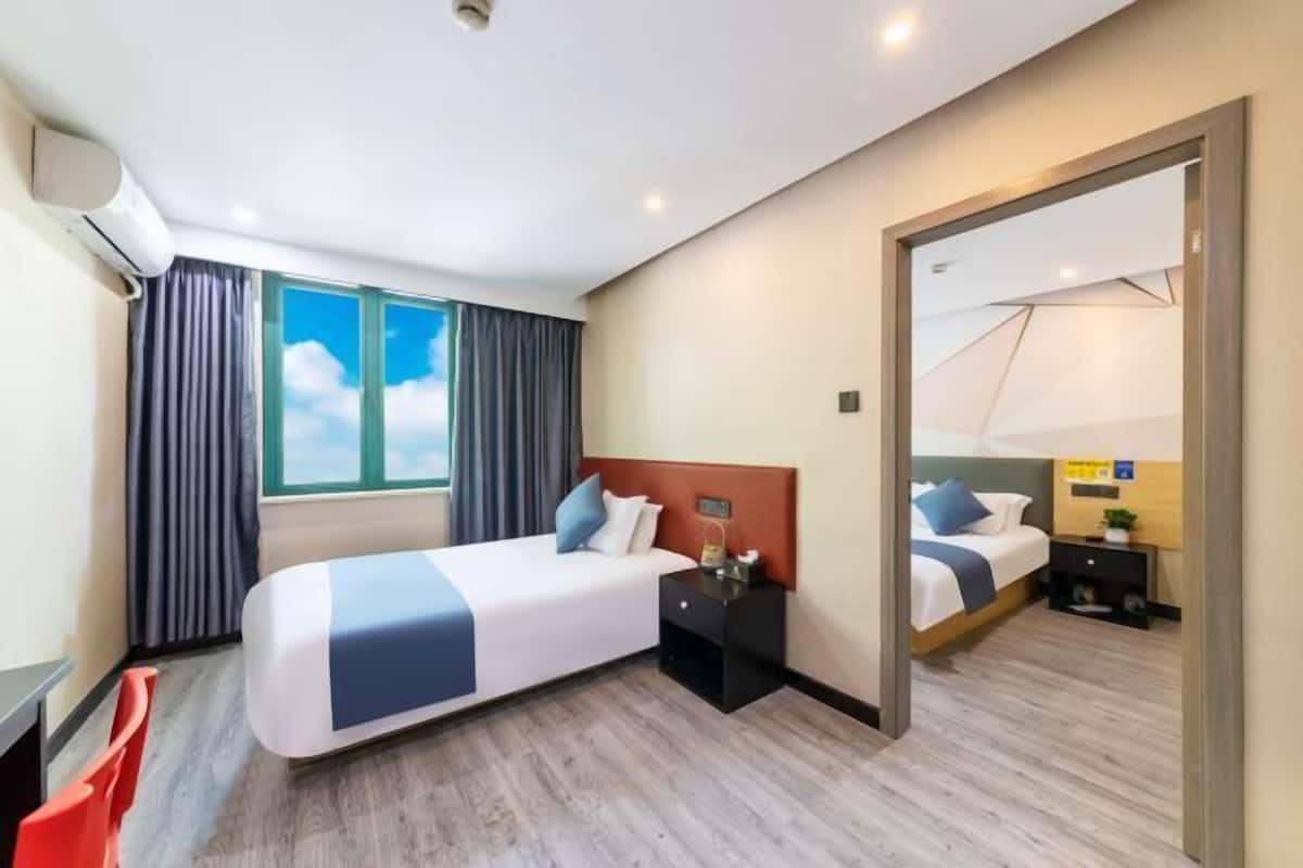 Una habitación de hotel con cama, mesita de noche, espejo y ventana con cortinas.