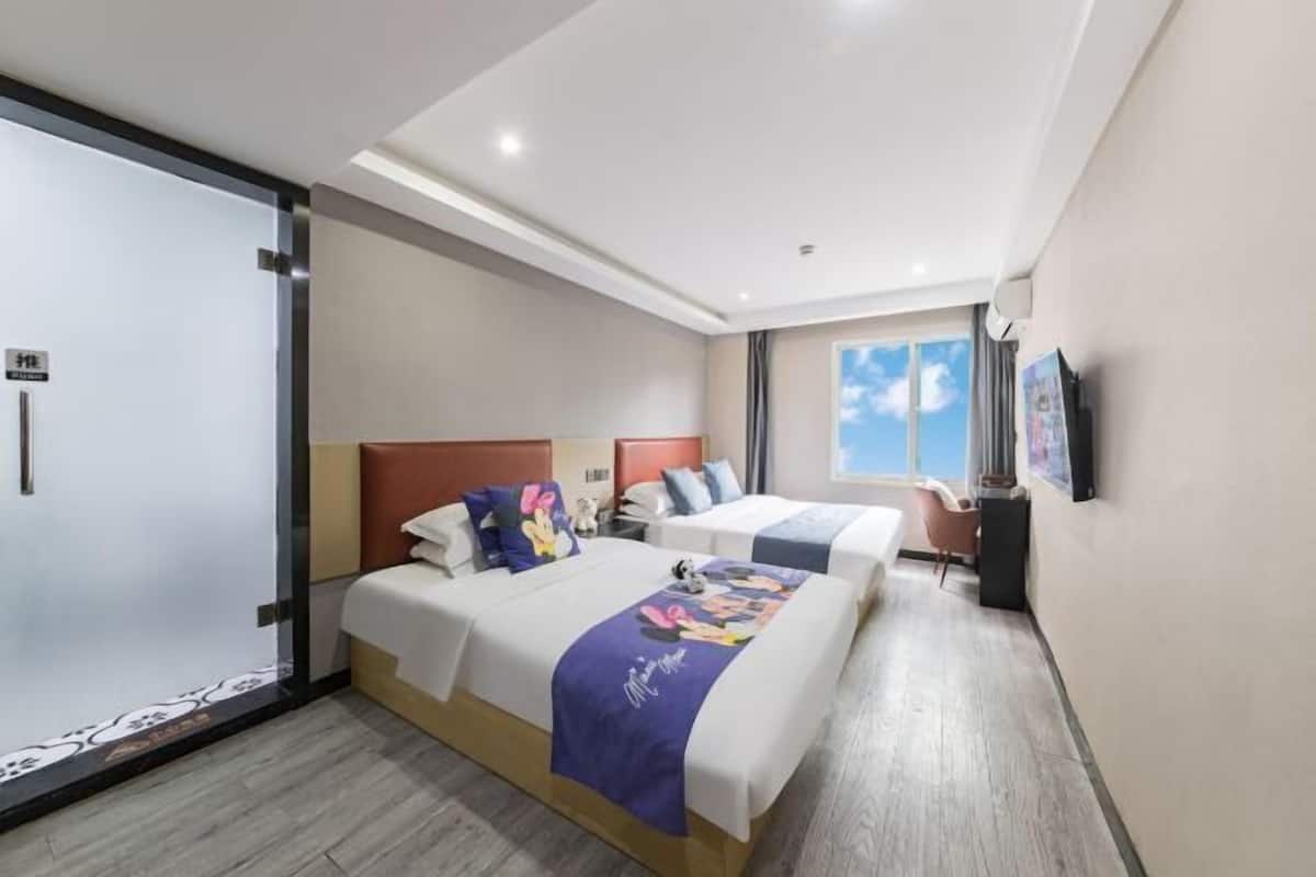 Habitación de hotel con dos camas, un ventanal grande, televisor de pantalla plana y puerta corredera.