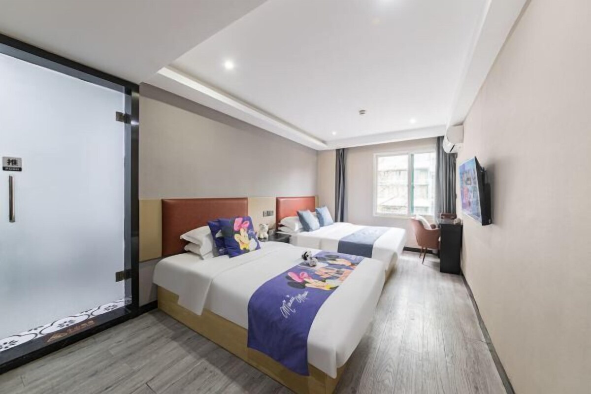 A hotel room with two beds, a large window, and a flat-screen TV on the wall.