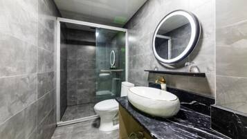 A modern bathroom with a glass-enclosed shower, a white toilet, and a marble sink with a round mirror.