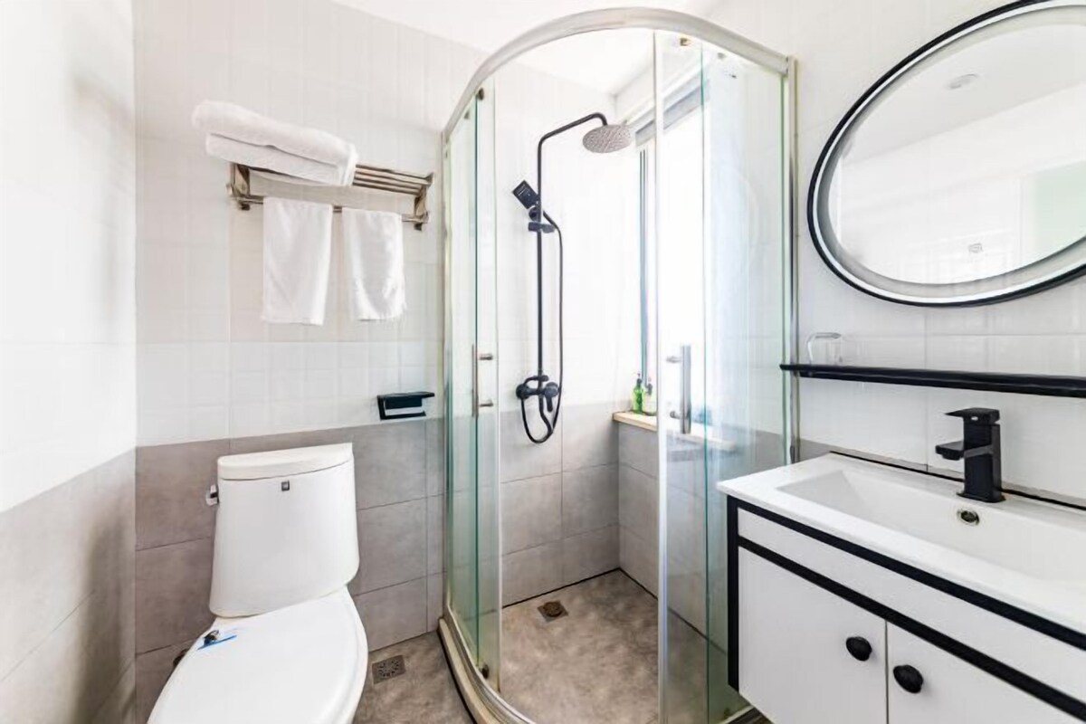 A modern bathroom with a glass-enclosed shower, a white toilet, and a white sink with a black faucet.