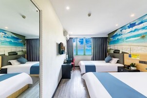 Habitación de hotel con dos camas, un escritorio, una silla, un ventanal con cortinas y un mural con una escena de playa.