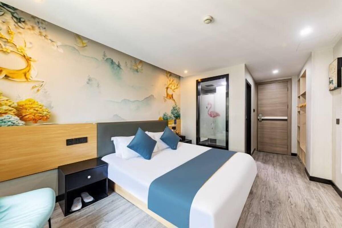 Habitación de hotel con cama, mesita de noche, una silla y una pared con un mural.