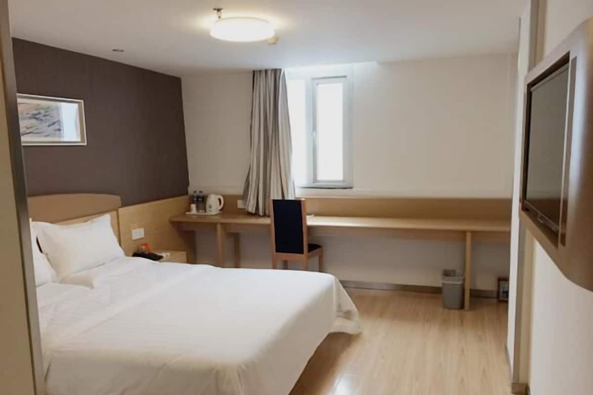 Una habitación de hotel con cama, escritorio, silla, ventana y televisión.