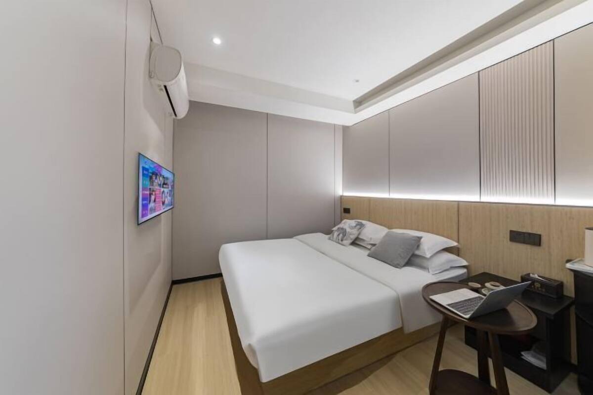 Una habitación de hotel moderna con una cama bien hecha, un escritorio con una computadora portátil y un aire acondicionado de pared.